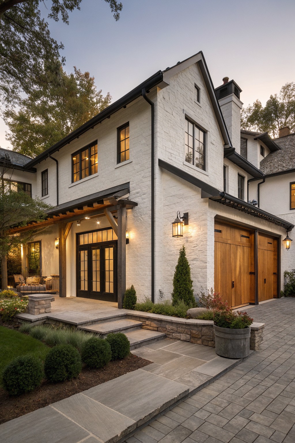 White brick house with wooden garage doors, stone steps, and evening lighting.