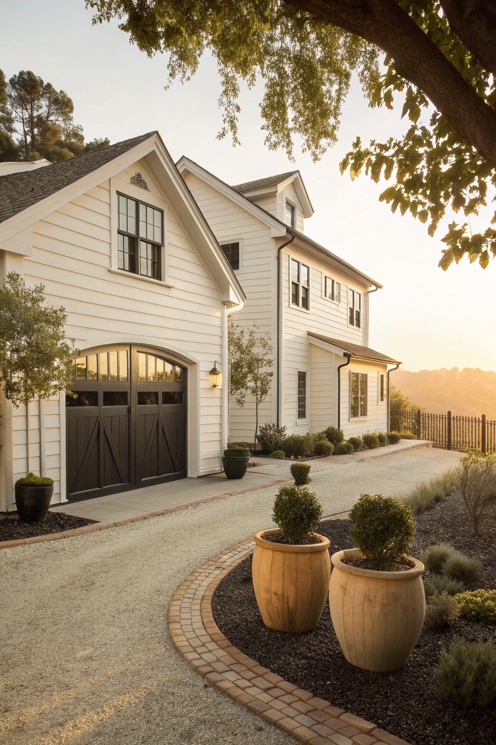 A white two-story house with dark garage doors under an arched opening, multiple gables, and large wooden planters along a curved driveway.