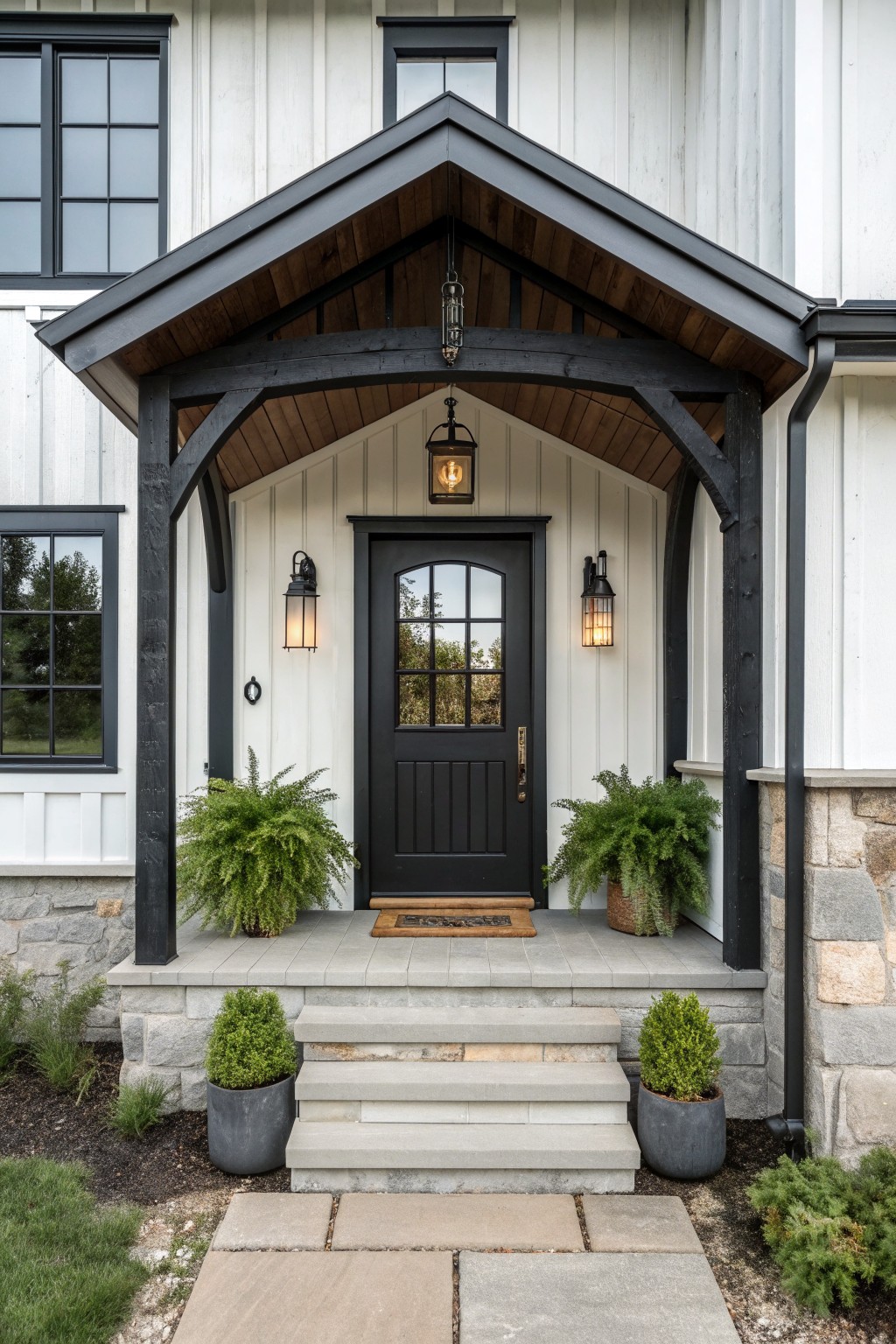 Black door under gabled porch with lanterns, ferns in pots, and stone steps.