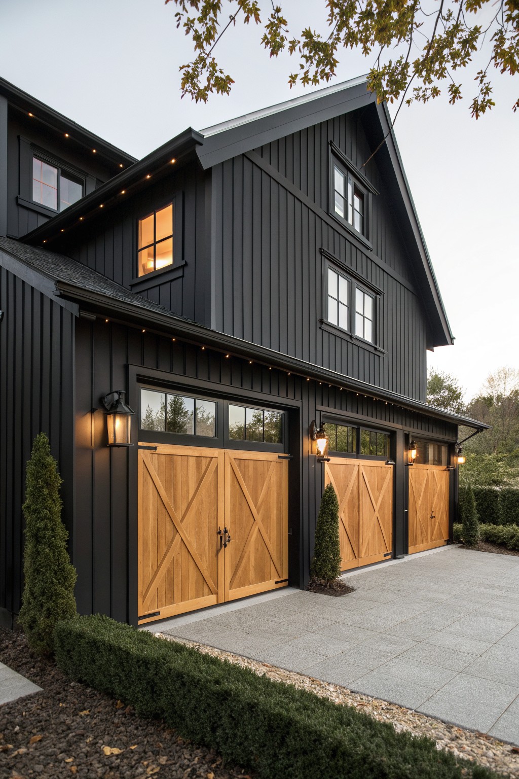 A matte black two-story farmhouse exterior with light wood garage doors, black-framed windows, and string lights along the roofline.