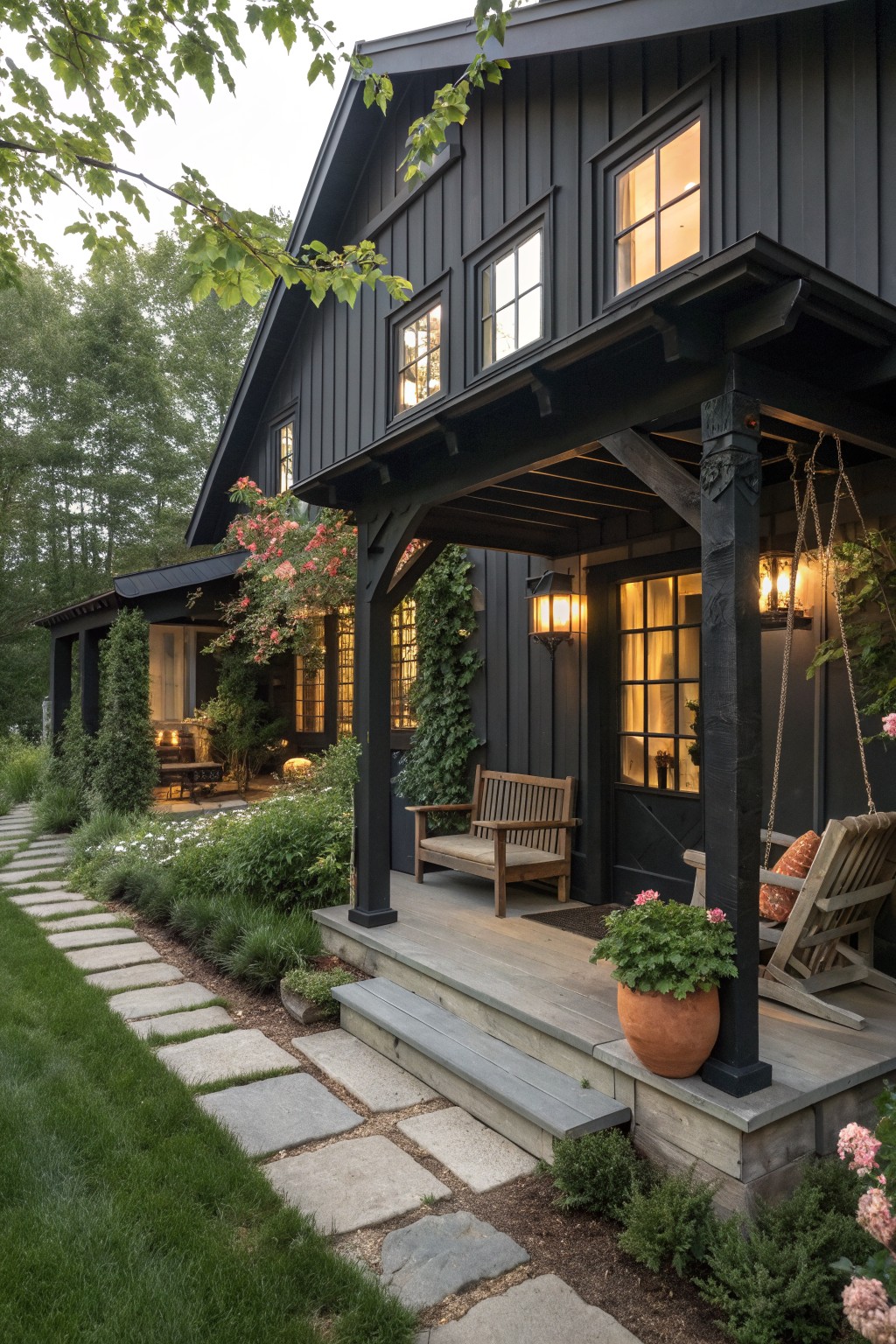 A matte black farmhouse exterior with vertical siding, a covered wooden porch, steps, and warm interior lighting visible through the windows.