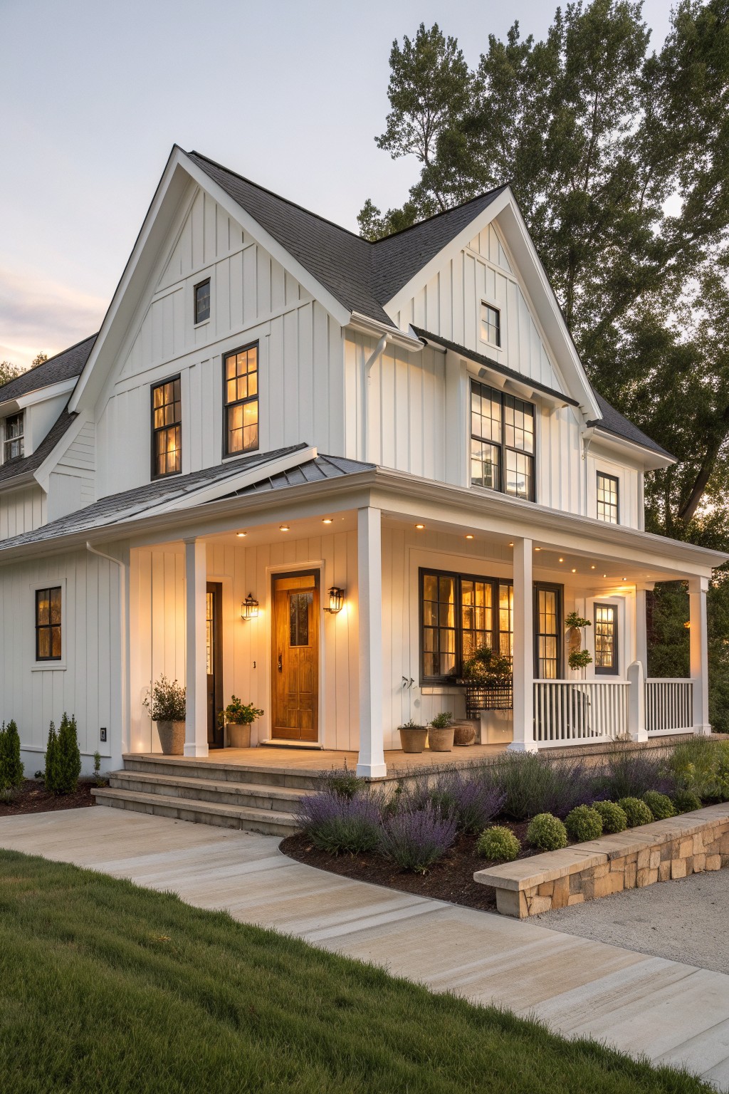 White two-story farmhouse with black roof, lit porch, and garden at dusk