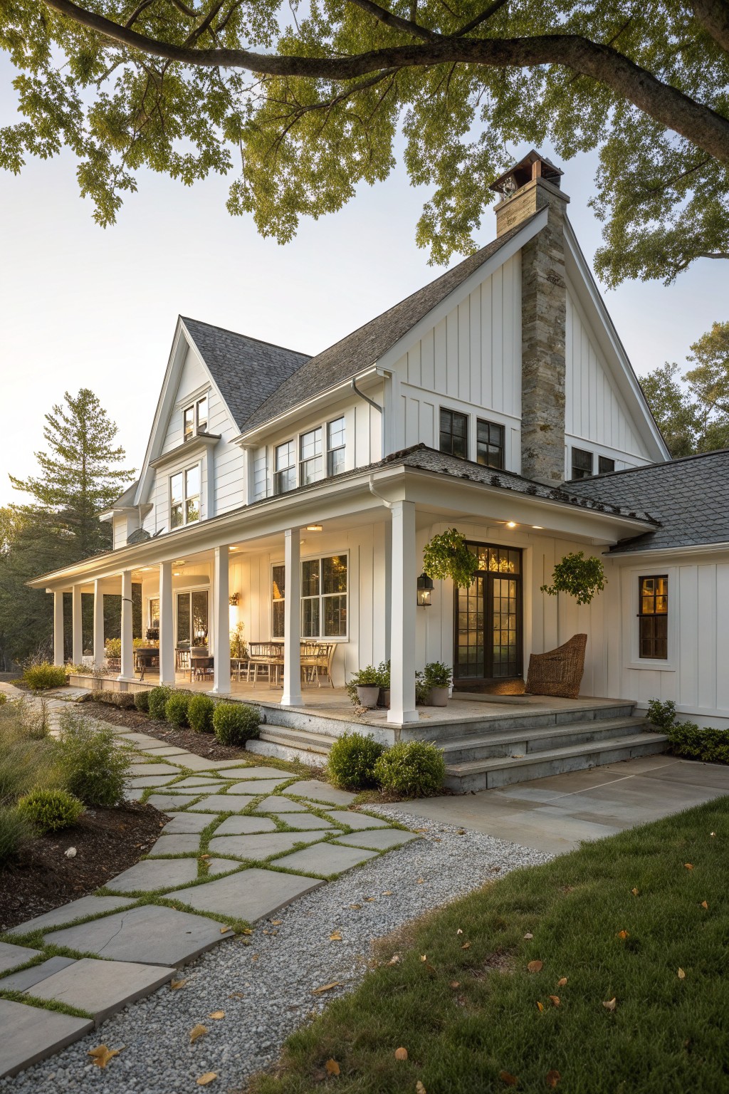 A white two-story farmhouse exterior with a tall stone chimney, covered front porch supported by white columns, and a stone pathway leading to the steps.