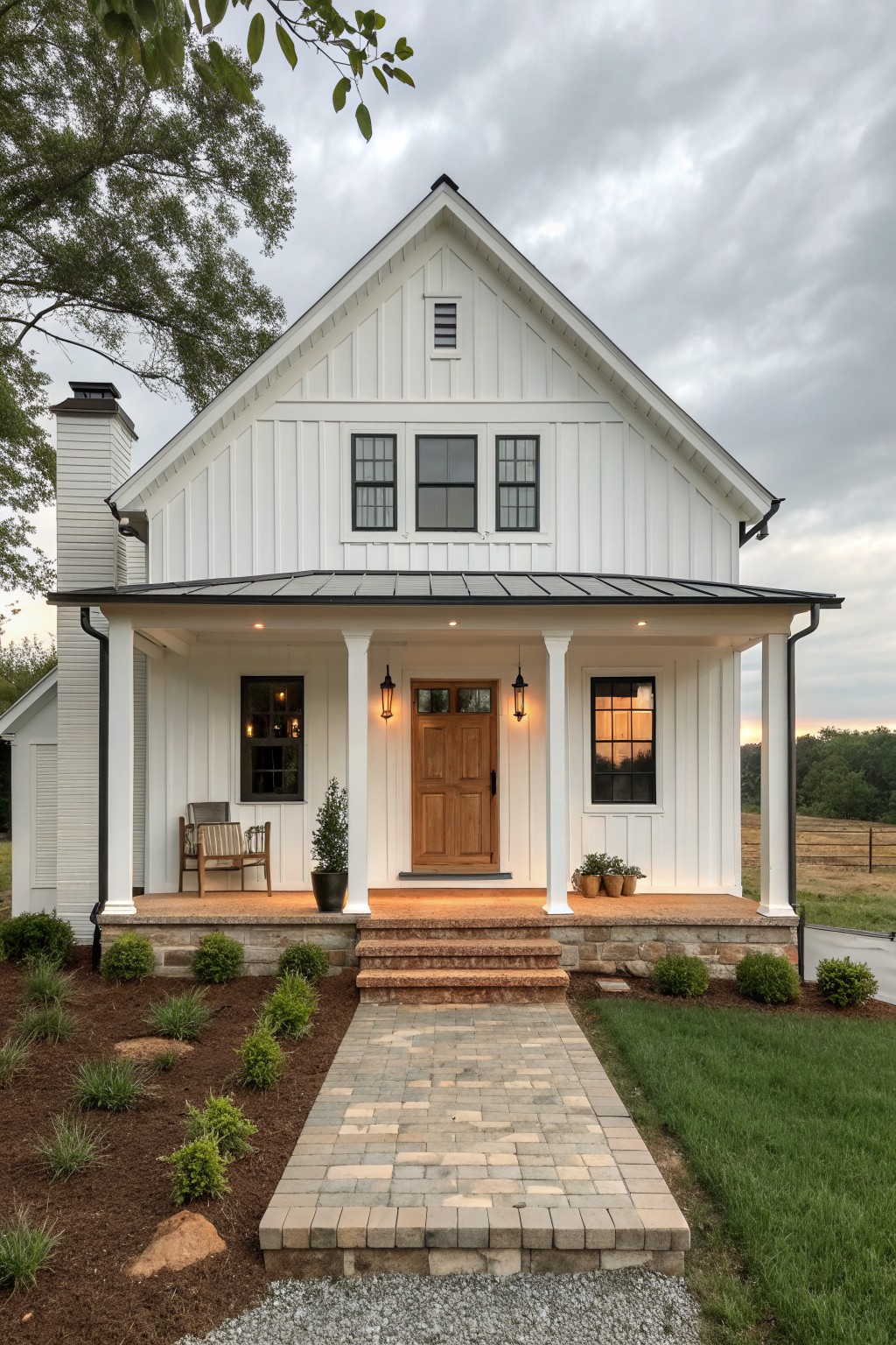 A white two-story farmhouse exterior with a gabled roof, covered porch supported by white columns, wooden front door, and stone foundation.