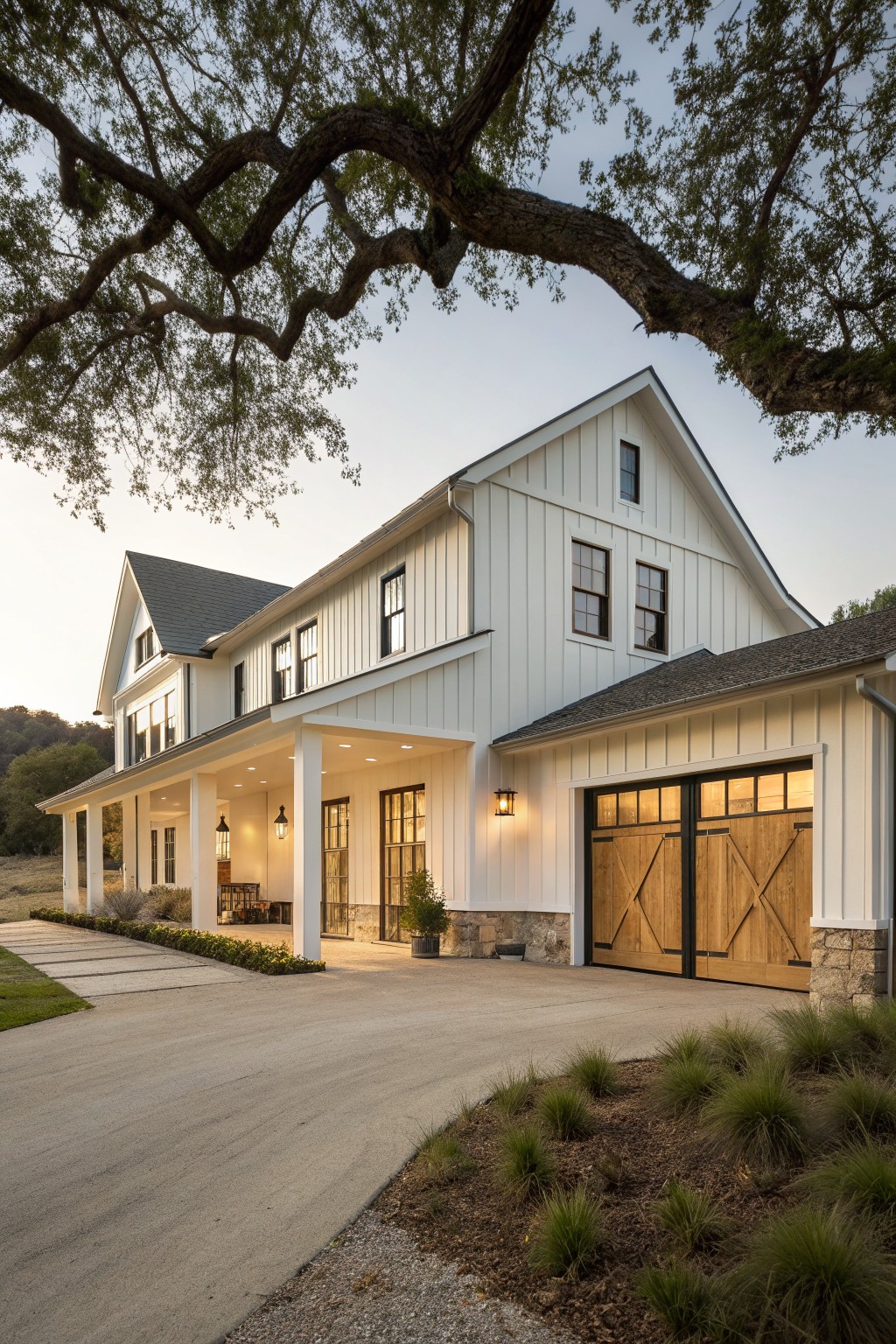 A white ranch farmhouse exterior with vertical board and batten siding, a stone foundation, wooden garage doors, and a covered porch.