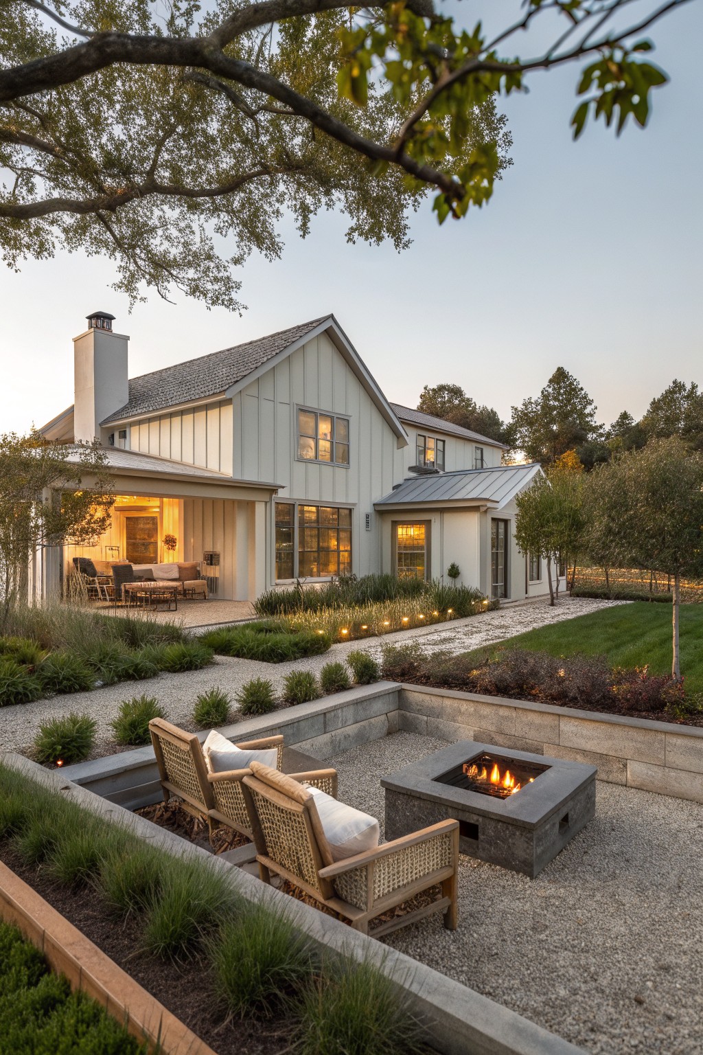 A light-colored ranch house with a gravel courtyard that includes a sunken concrete fire pit, woven chairs, and surrounding landscaping.