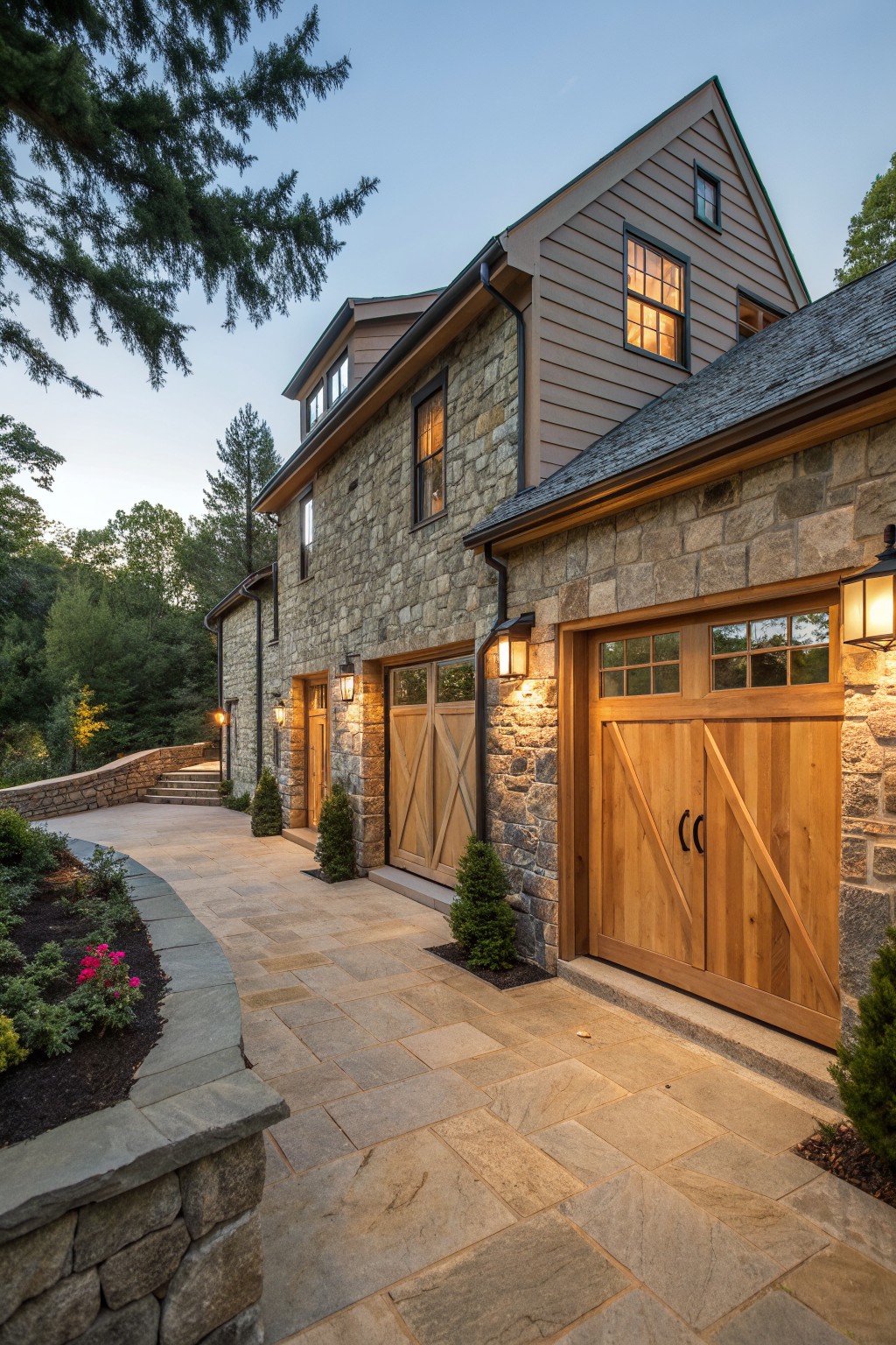 Stone house with wooden garage doors on curved paved driveway at dusk