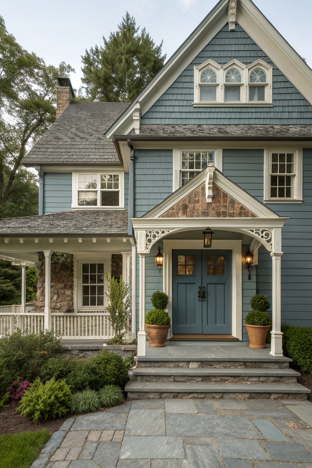 A two-story Victorian farmhouse with blue-gray siding, white trim, a gabled stone-accented entry porch, and a blue double front door.