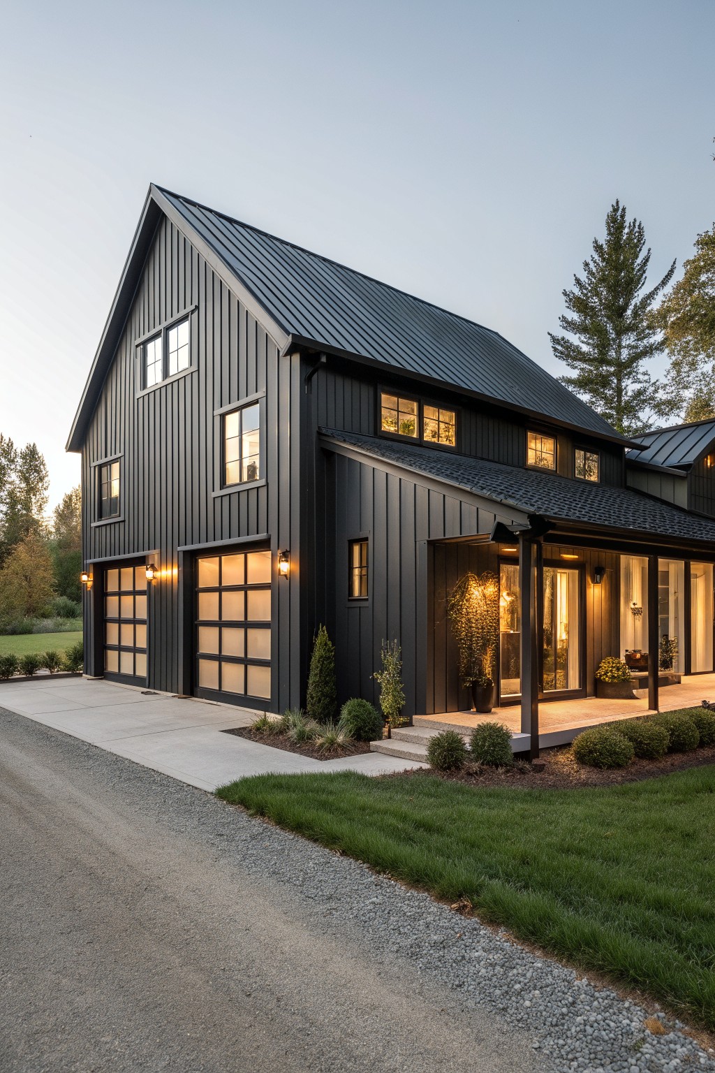 Modern black house with glowing windows, two garages, and covered porch at dusk