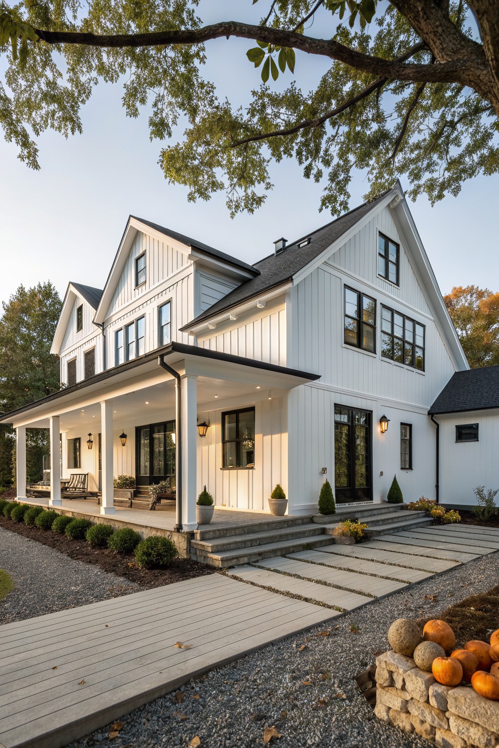 A white two-story barn-style house with black-framed windows, a wide covered porch, stone steps, and gravel paths in front.