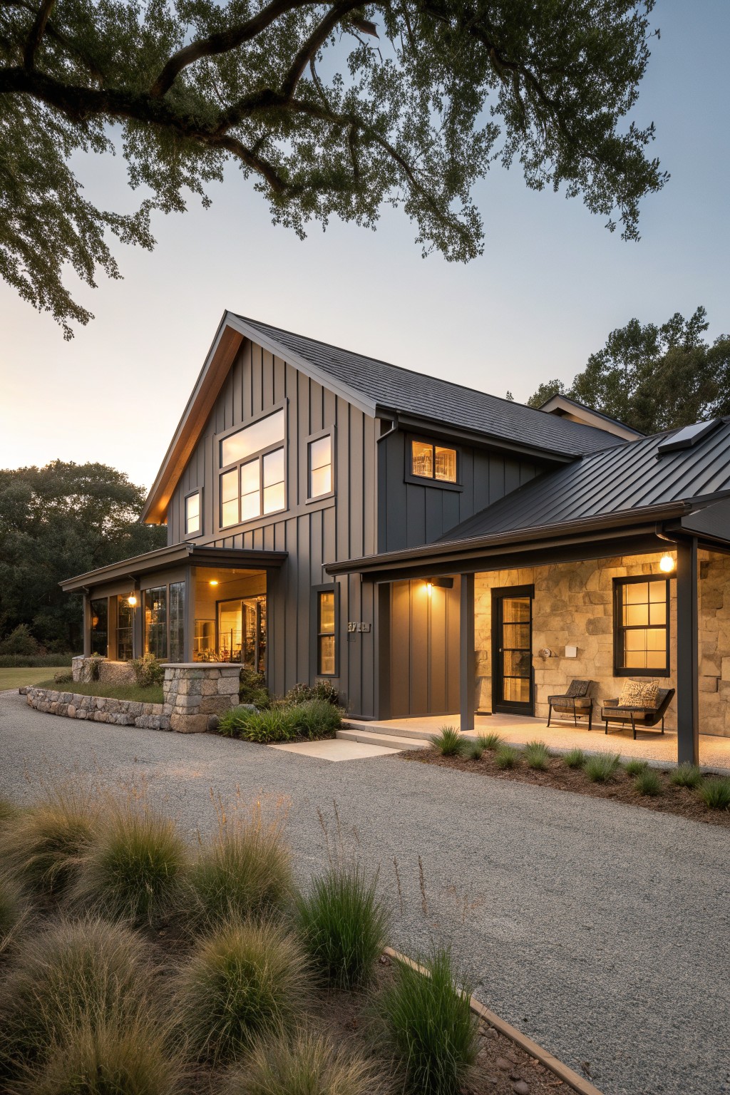 A single-story farmhouse exterior with dark gray vertical siding, a black metal roof, stone accents on the right, and a gravel driveway in the foreground.