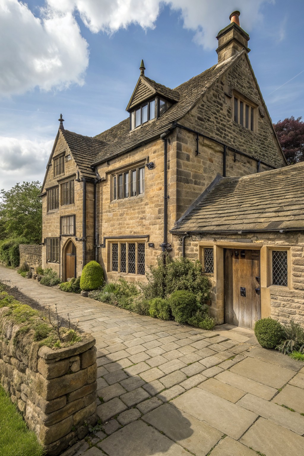 A large stone house with multiple gabled roofs, wooden doors, and a paved pathway leading to the entrance.