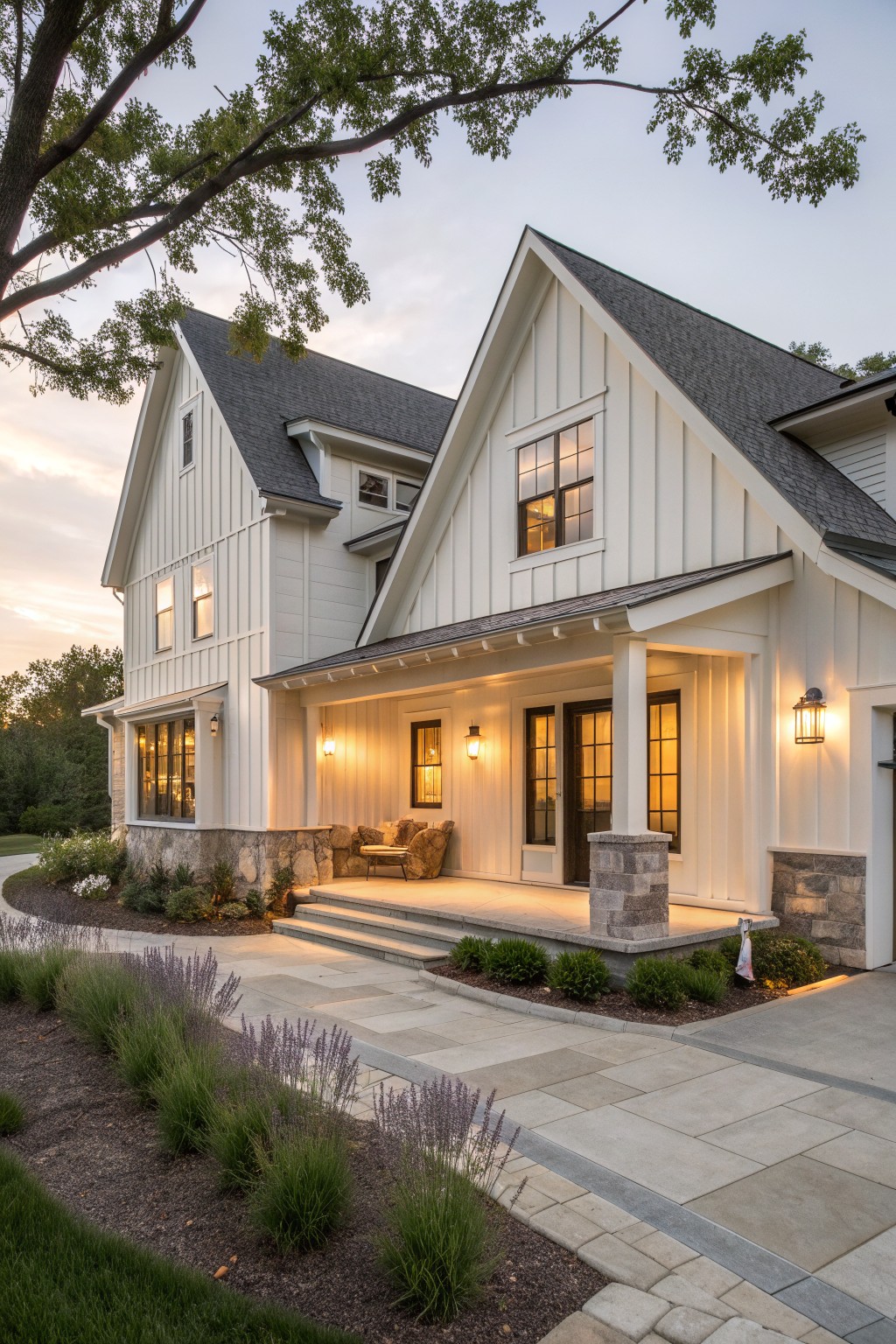 White two-story farmhouse with stone pillars, lit porch, and landscaped front yard at dusk.
