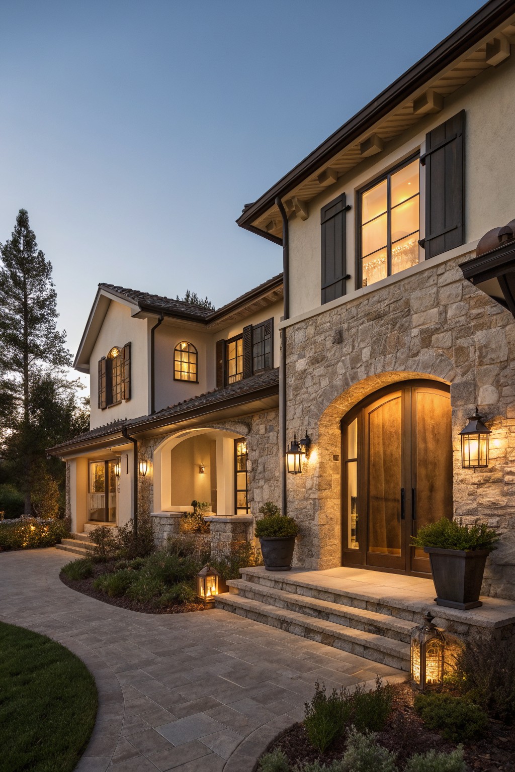 Luxurious two-story stone house with arched entry, glowing windows, and lanterns at dusk.