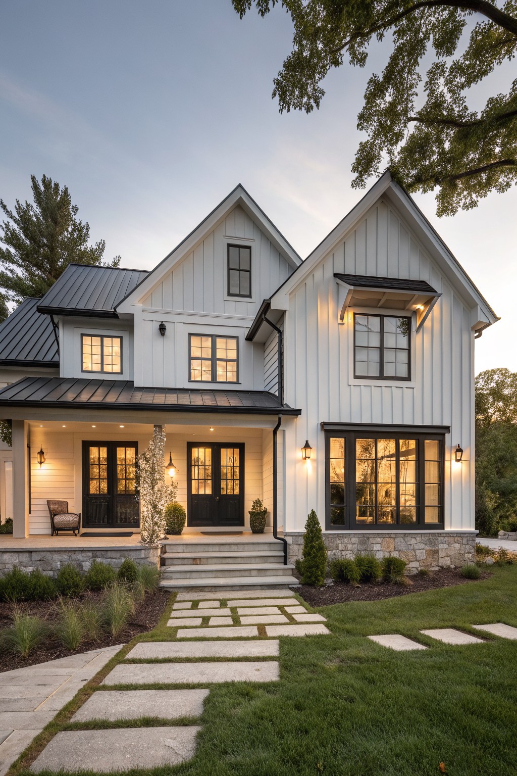 A white two-story modern Victorian farmhouse with black-framed windows and doors, gabled roofs, stone foundation, and a covered front porch.