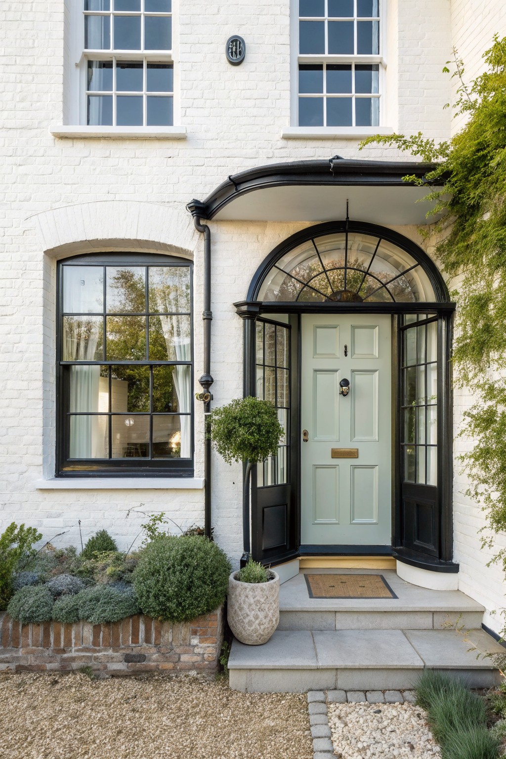 Front view of a white brick house with a light green door centered under a black arched canopy and framed by black-trimmed sidelights and transom.