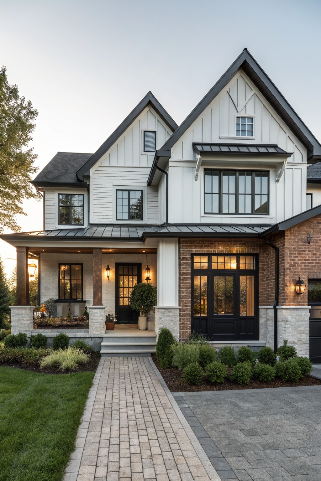A two-story modern farmhouse exterior with white siding on the gables, red brick on the lower right wall, black-framed windows and doors, a covered front porch with stone columns, and a brick walkway leading to the entrance.