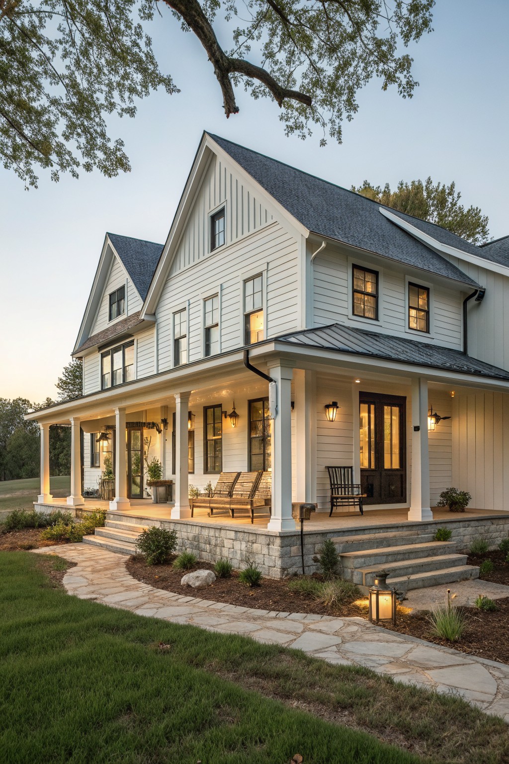 White two-story farmhouse exterior with dark roof, multiple gables, and a front porch supported by white columns resting on a stone foundation.
