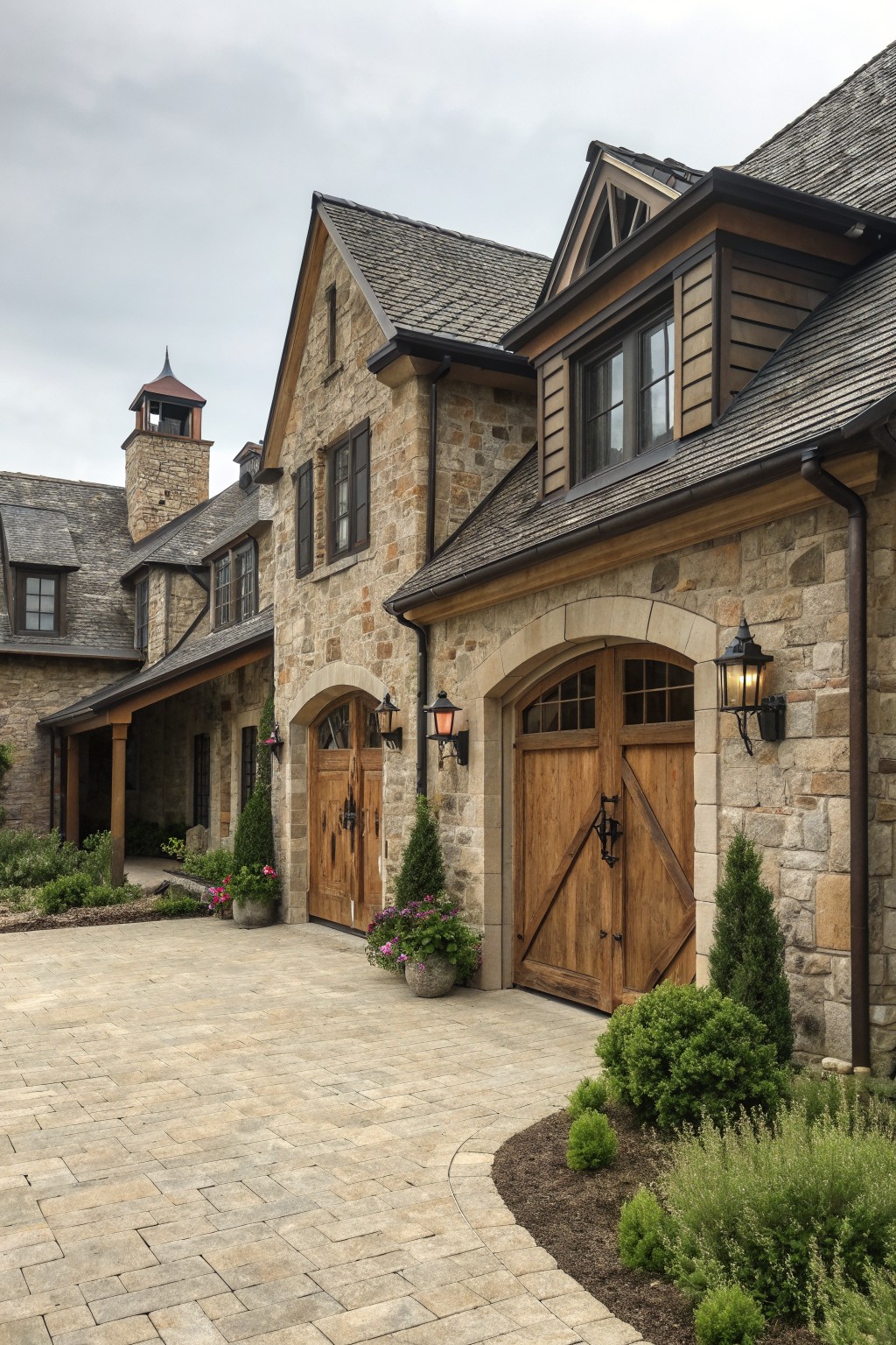 Stone farmhouse exterior showing two wooden garage doors beneath arched openings with black lanterns on either side.