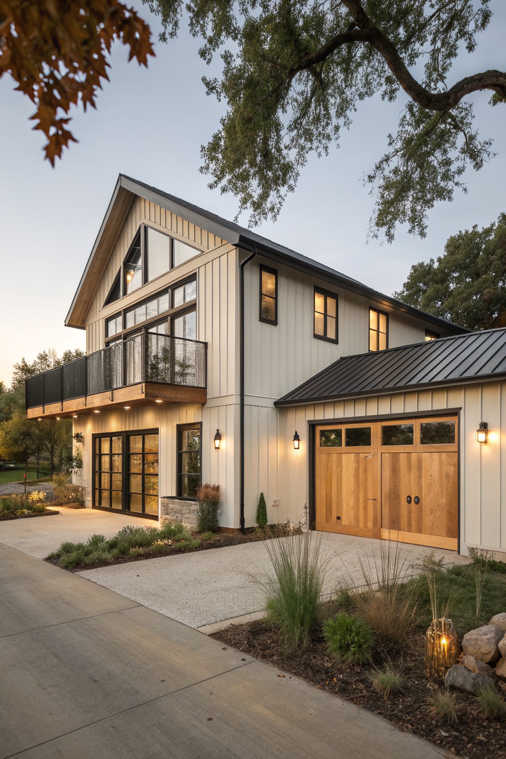 A two-story house with light vertical siding, a dark metal roof over the garage section, wooden garage doors, and a second-floor balcony with metal railing.