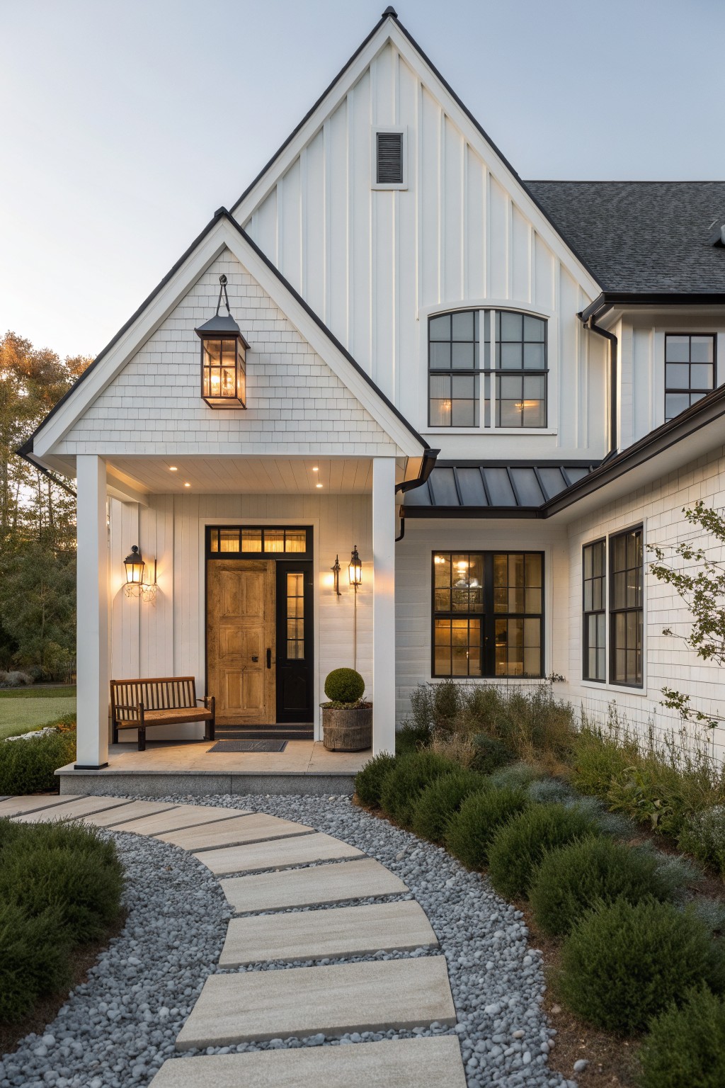 Front view of a white modern farmhouse with a gabled porch, wooden front door, black-framed windows, and a gravel path leading to the entrance.