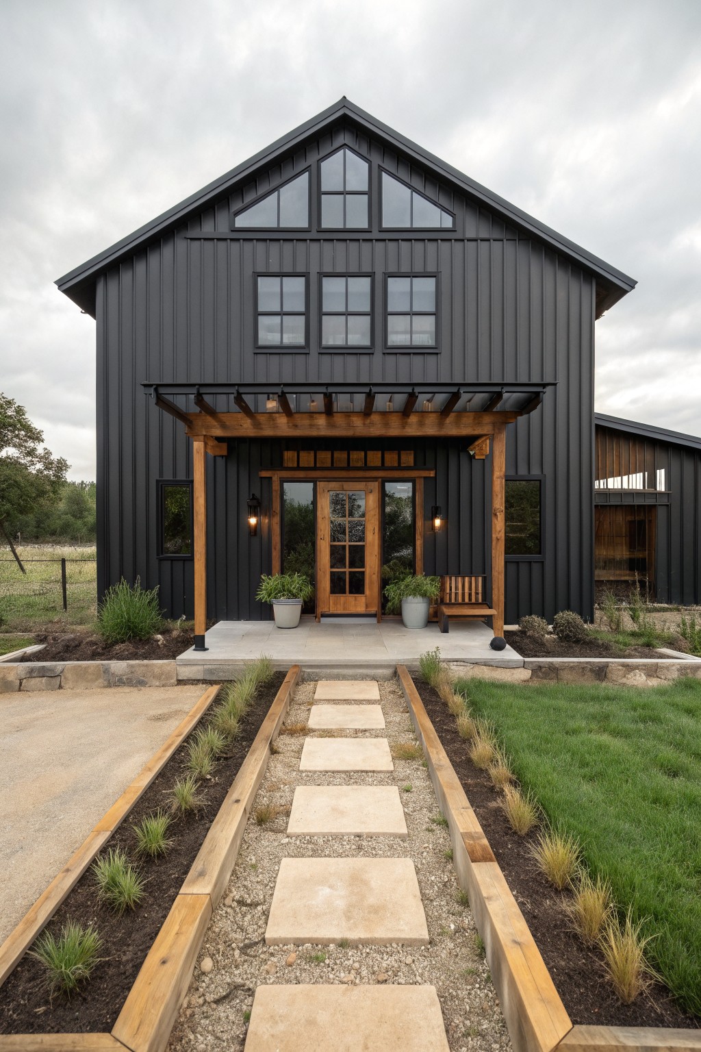 A black barndominium exterior with wooden porch supports and a pergola over the front door, plus a stone pathway leading to the entrance.