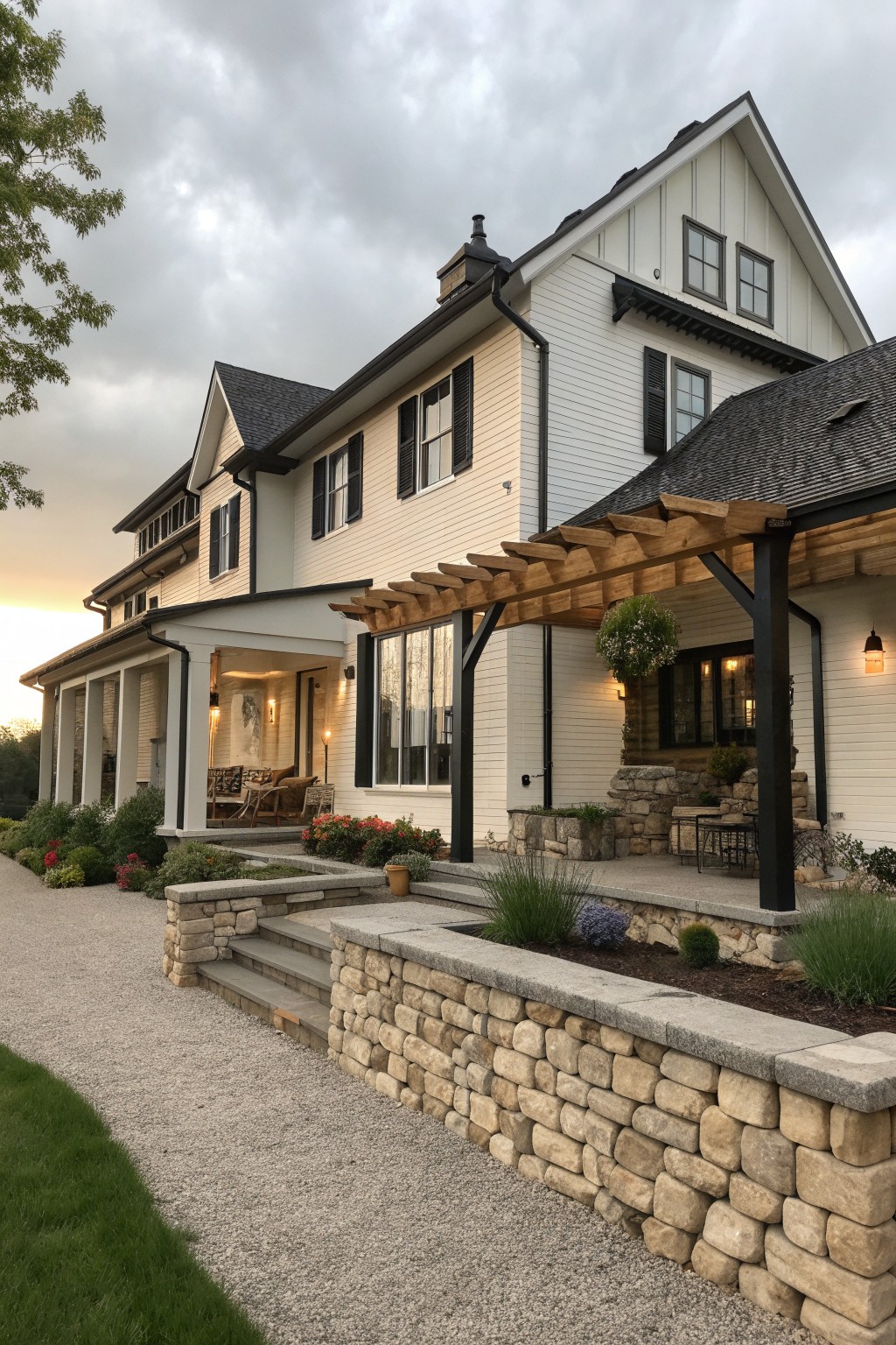 A white two-story farmhouse with black trim and shutters, a wooden pergola over the porch, and a stone retaining wall bordering a gravel driveway.