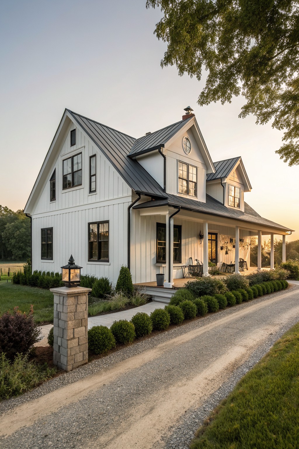 A white two-story farmhouse with a dark metal roof, front porch, and gravel driveway lined with shrubs.
