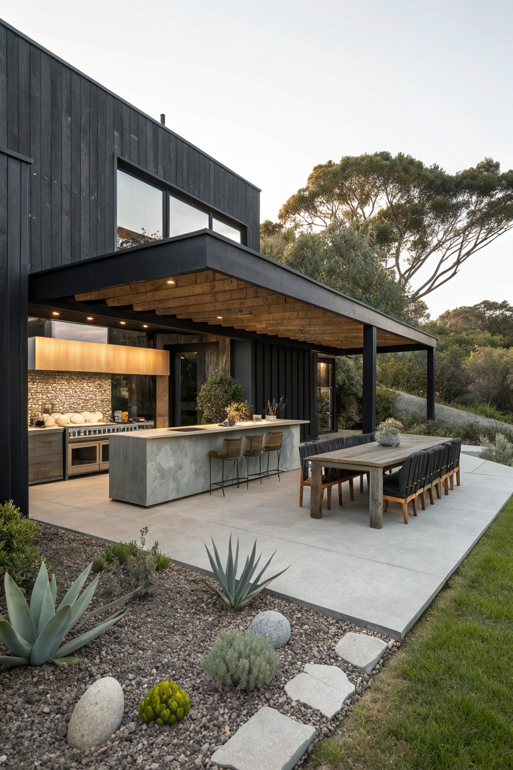 Modern black home with outdoor concrete kitchen island and long wooden dining table