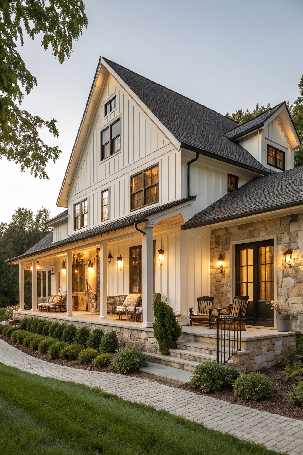 A two-story white farmhouse with vertical siding, stone foundation and porch walls, dark roof, covered porch, and stone steps leading to the entrance.