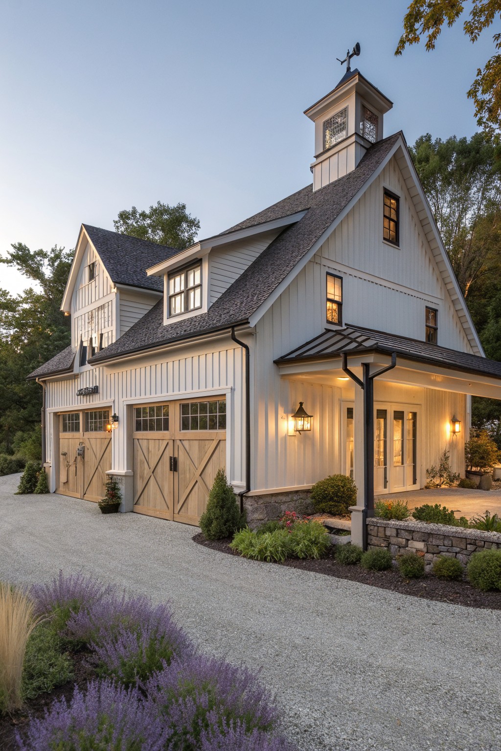 A white Victorian farmhouse with a tall cupola on the roof, multiple gables, and wooden carriage-style garage doors along a gravel driveway.