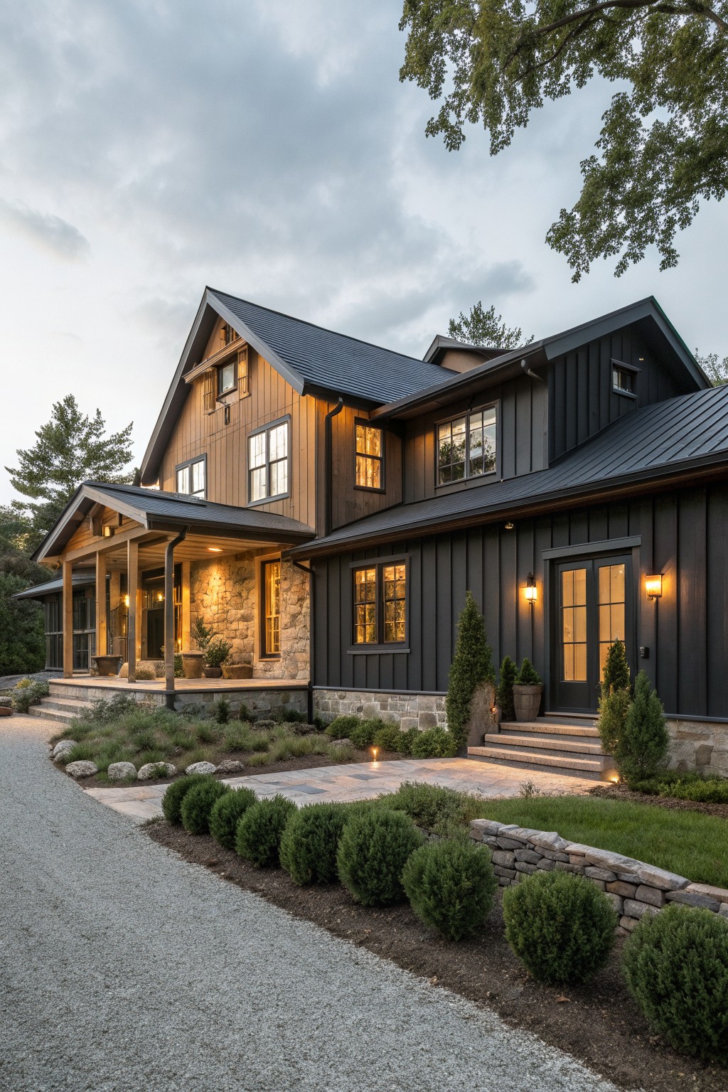A two-story farmhouse exterior with dark siding, cedar wood on the gables and porch, stone foundation, and a gravel driveway in front.