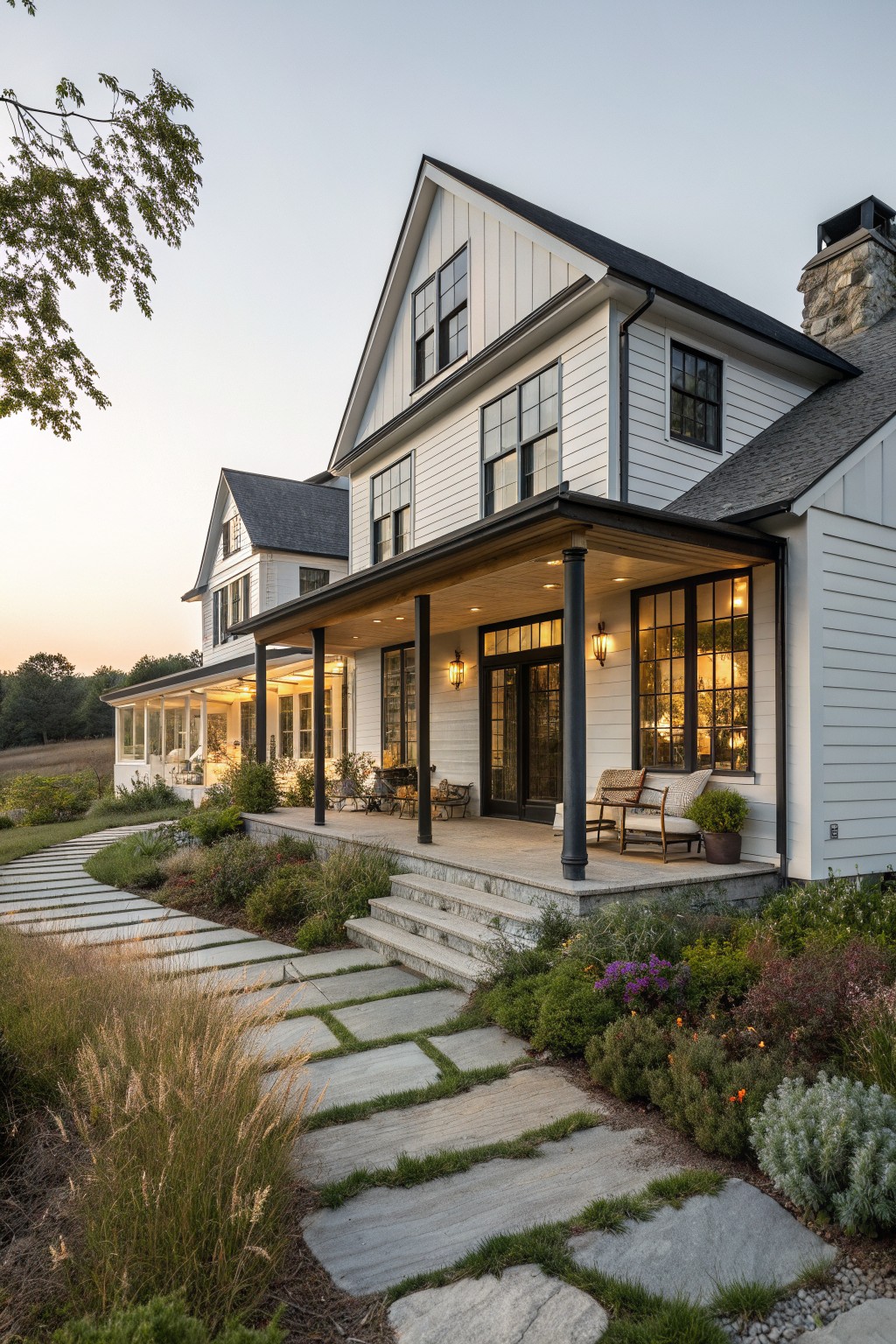 Modern white farmhouse with black windows, covered porch, stone steps, and garden path at dusk.