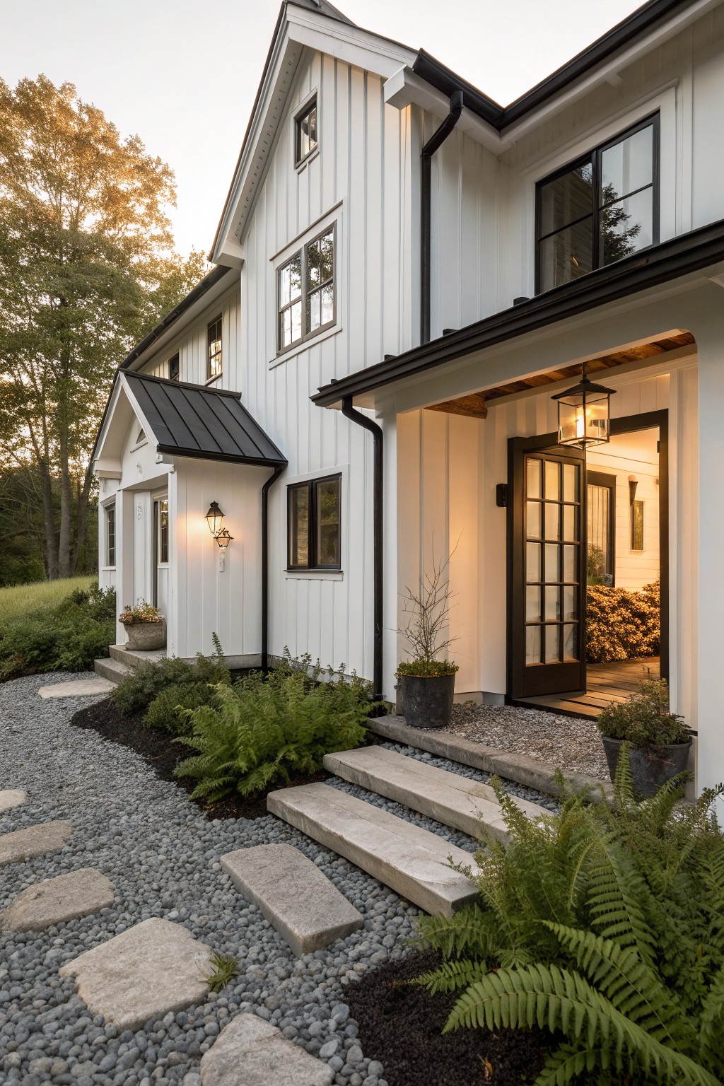 A white modern farmhouse exterior with vertical siding, dark-framed windows, a dark front door, and concrete steps bordered by gravel and ferns.