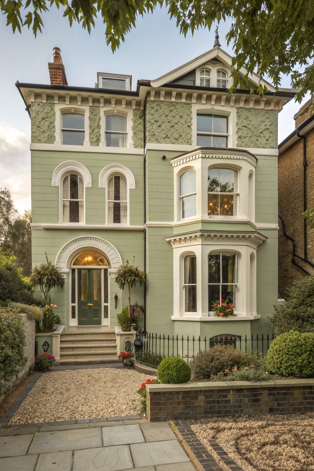A three-story Victorian house with sage green siding, white trim, a bay window, and a green arched front door.