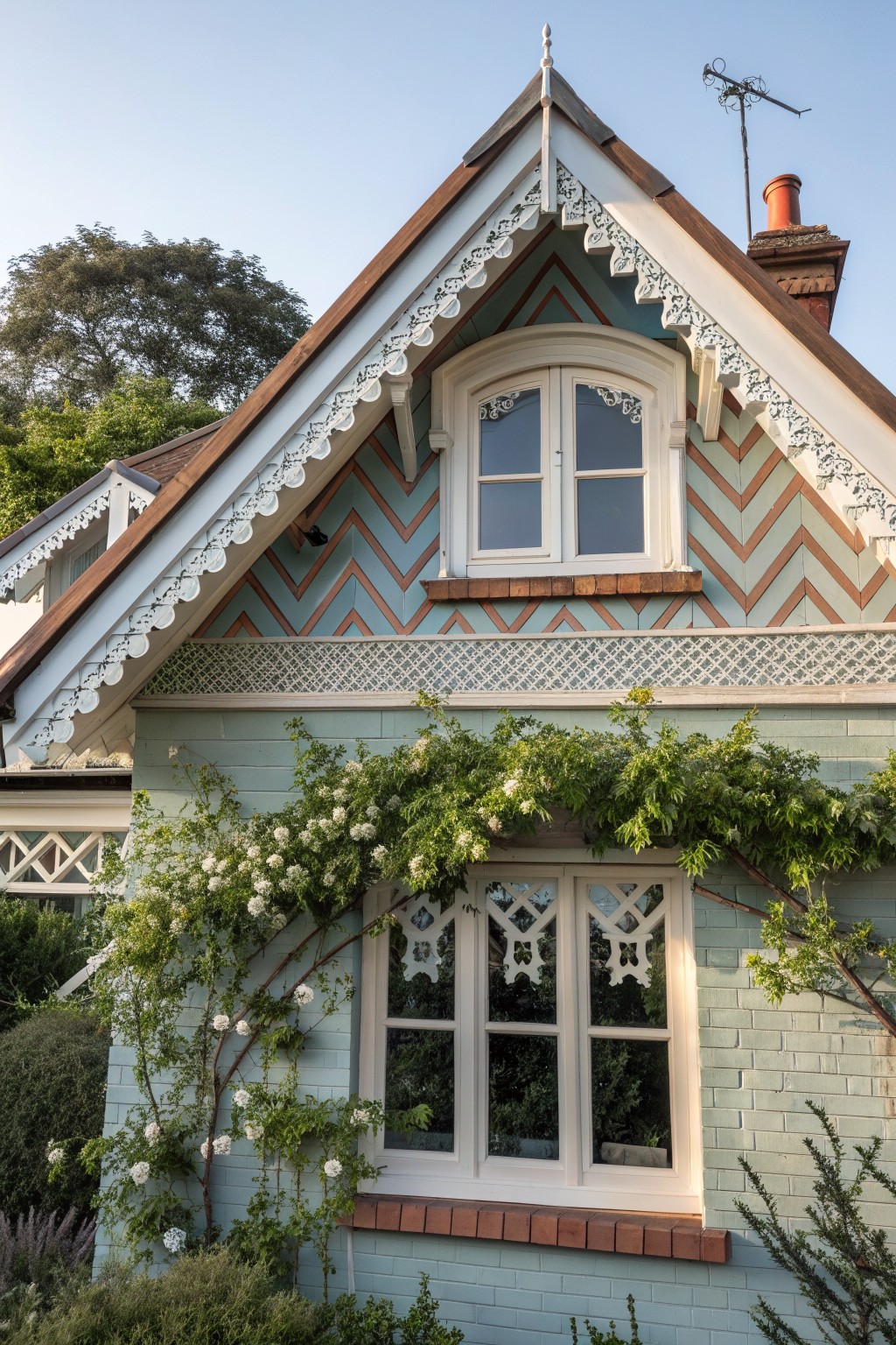 A close view of a Victorian farmhouse gable with chevron patterned siding in light blue and brown, white decorative bargeboard trim, and a centered window.