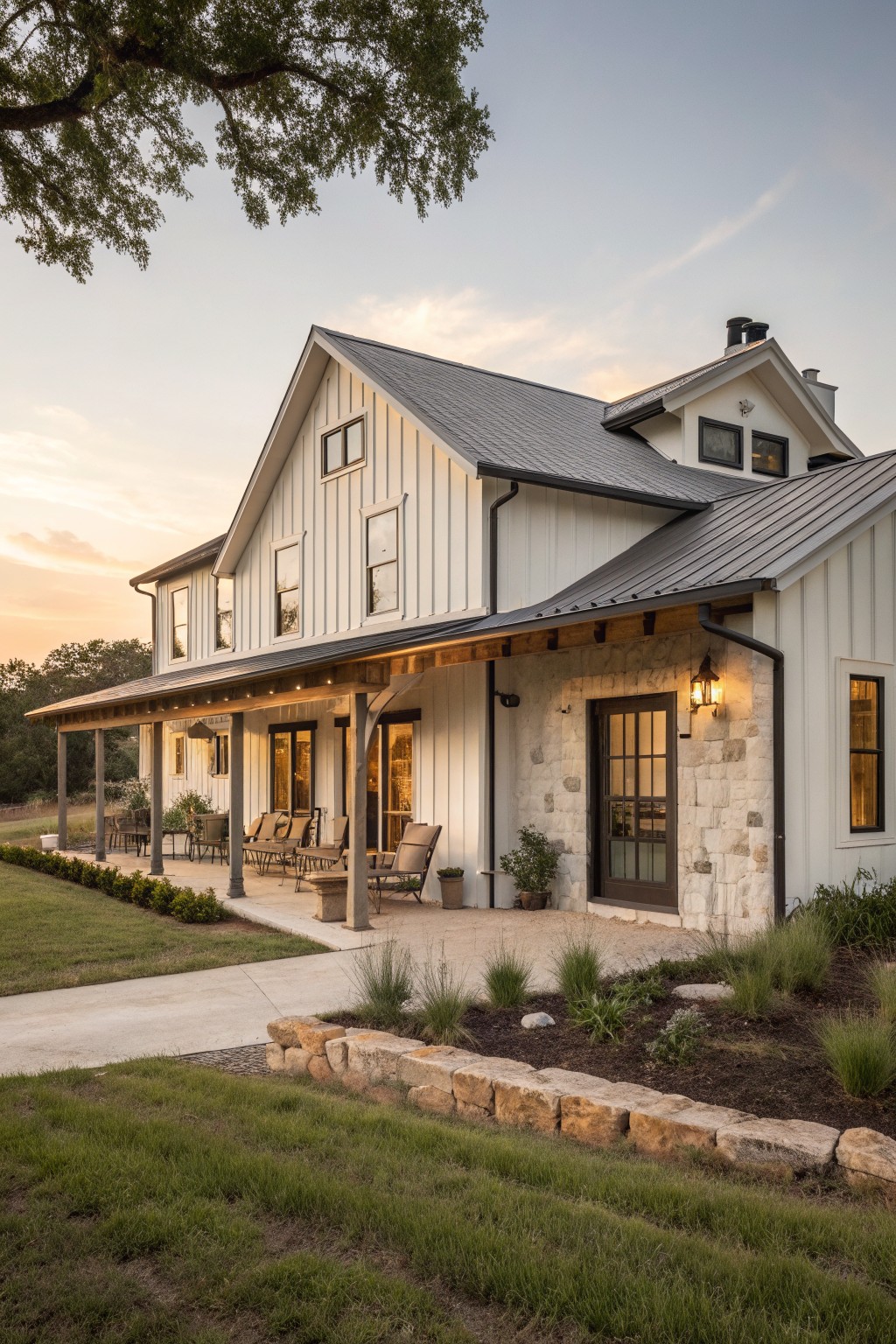 Modern white farmhouse with stone accents, covered porch, patio seating, and dusk lighting.