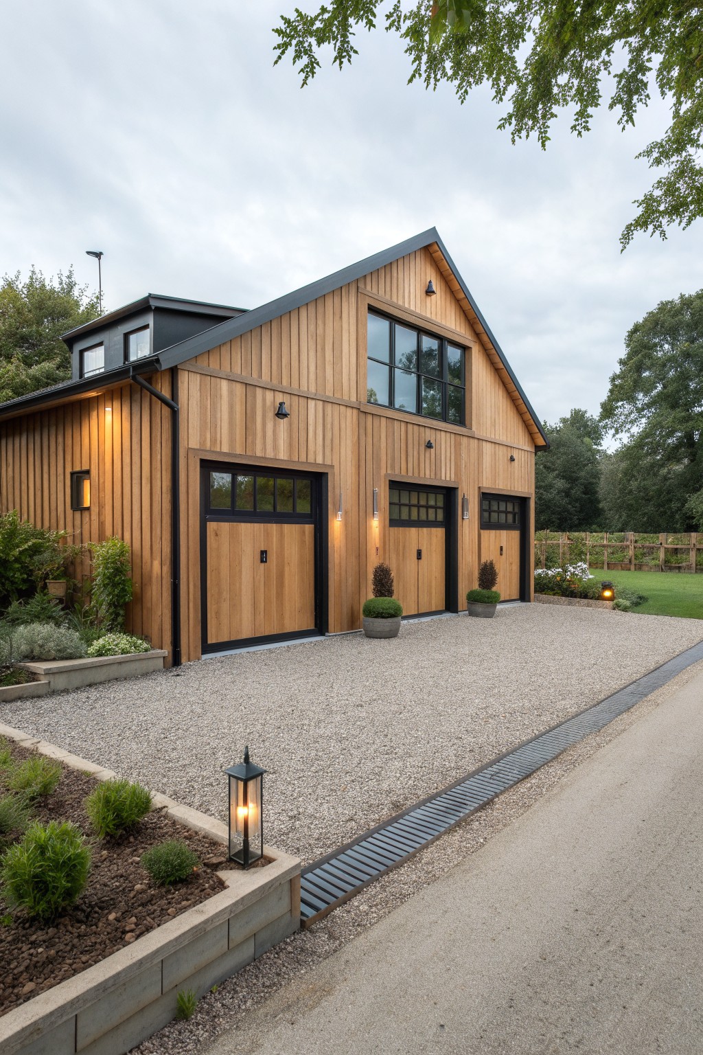 A two-story house with light wood horizontal siding, black-framed garage doors of varying sizes, and black window trim on a gravel driveway.