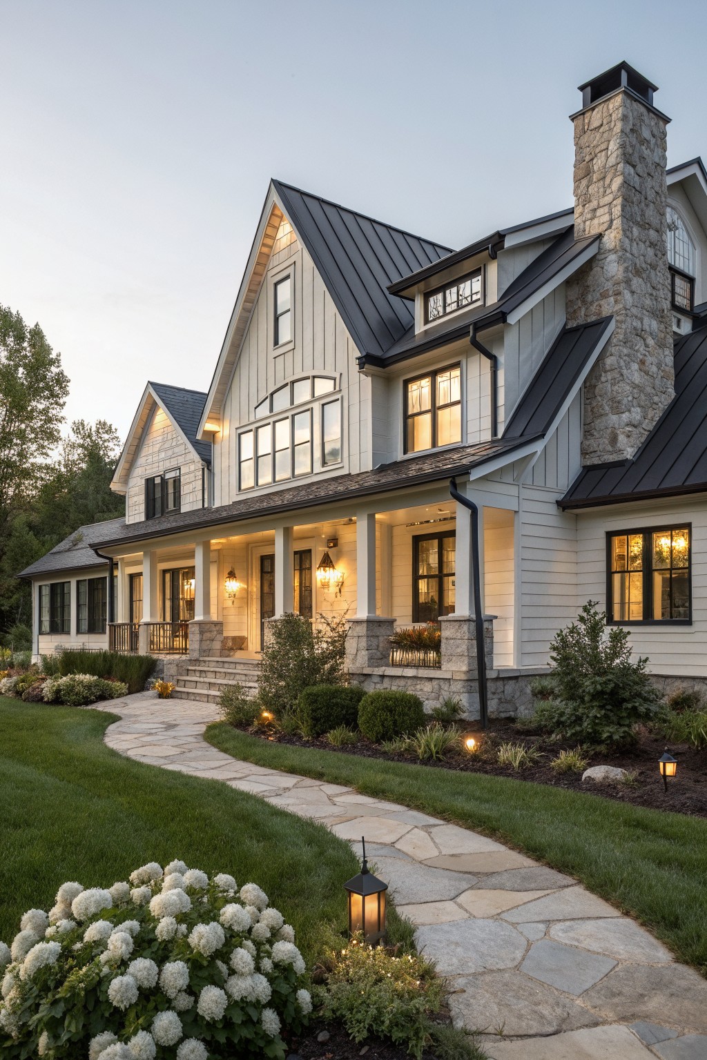 Large white house with black roof, stone chimney, lit porch, and winding stone path