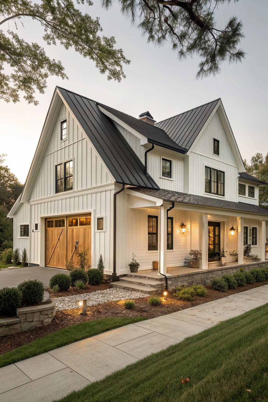 A white two-story farmhouse with a black metal roof, multiple gables, wooden garage doors on the left, and a covered porch with stone steps.