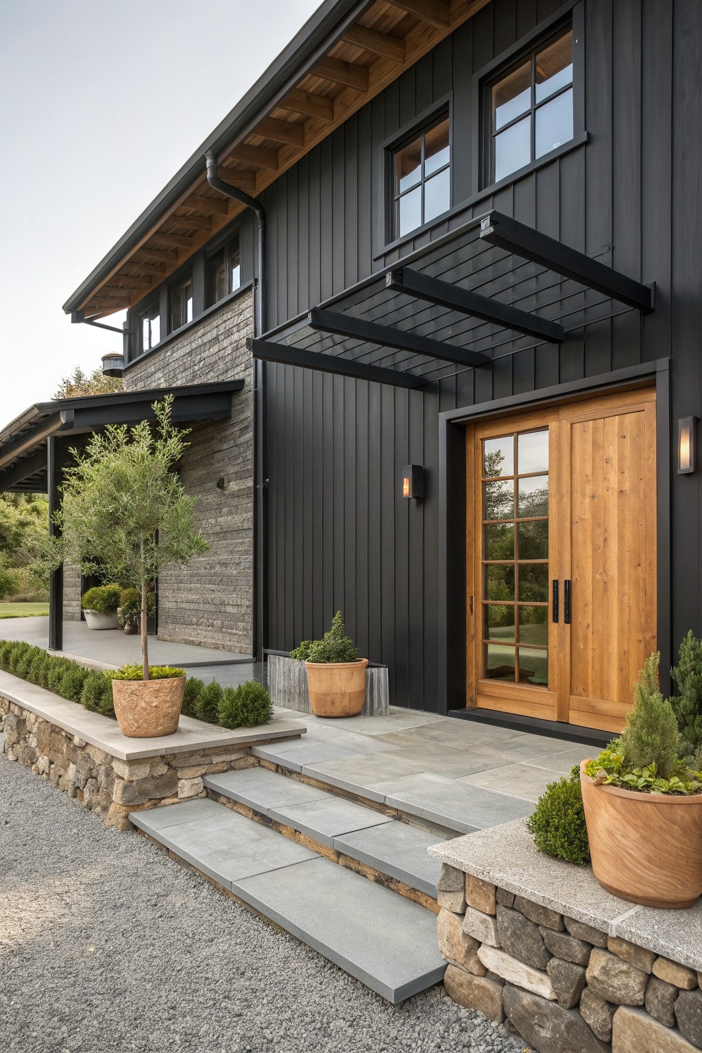 Modern black house with wooden doors, metal awning, stone steps, and potted plants.