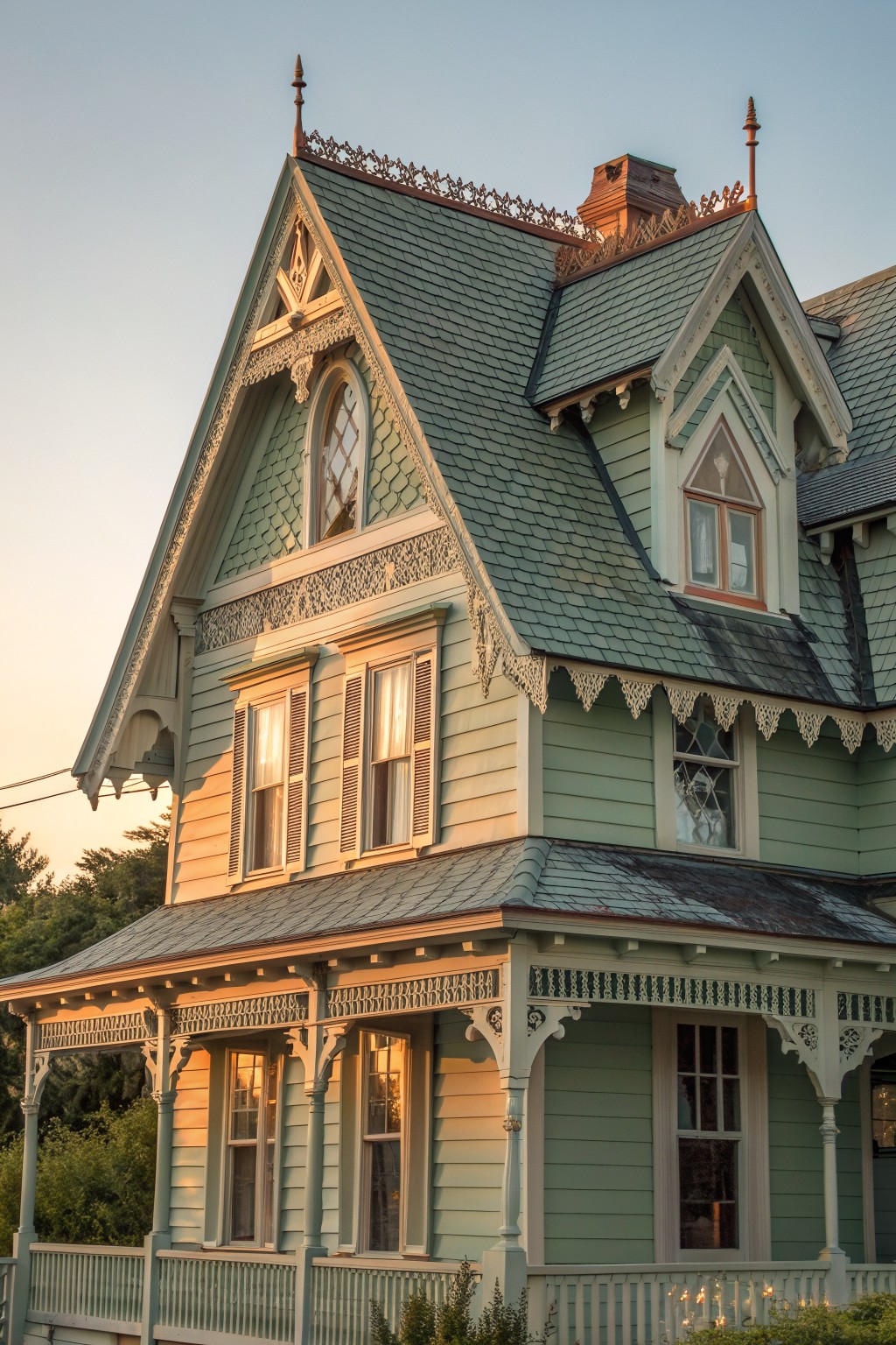 Ornate Victorian house with pale green siding, steep roof, and intricate trim at sunset.