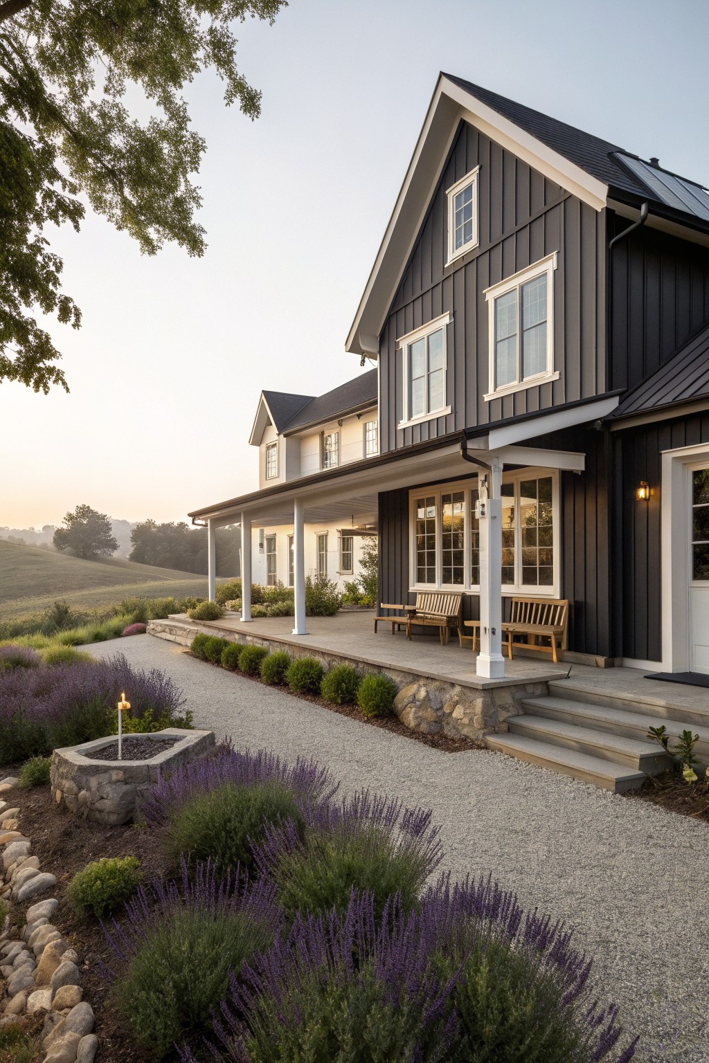 A modern farmhouse with dark gray vertical siding, white trim around the windows, a covered porch with wooden benches, and lavender plantings along the gravel path.