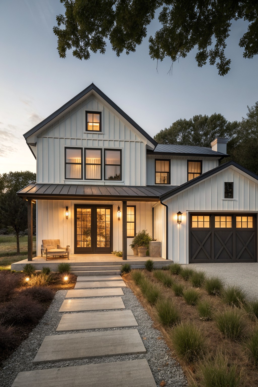 Modern white farmhouse with black trim, lit porch, garage, and stone path at dusk
