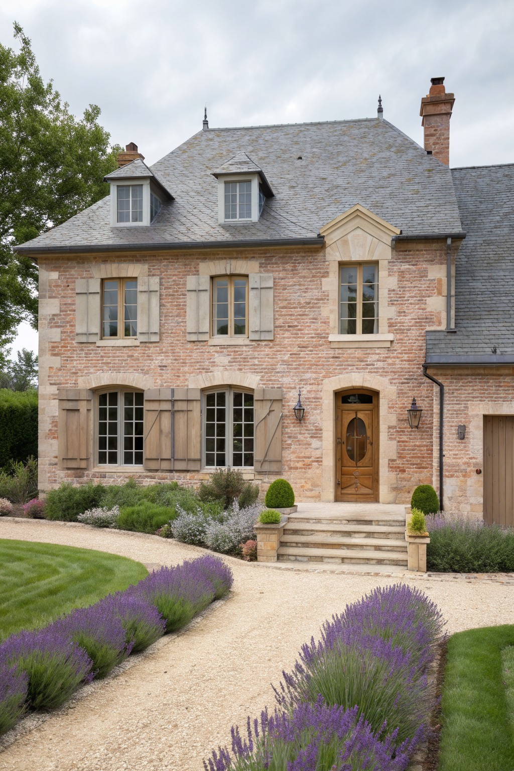 Elegant brick French house with gray slate roof, dormers, and lavender-lined gravel drive.
