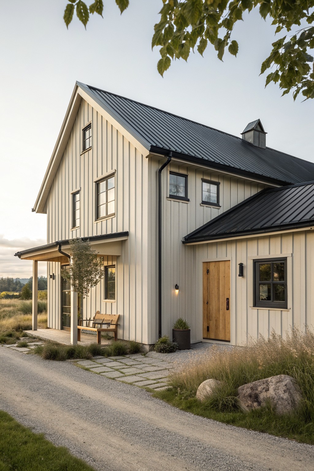 Modern white farmhouse with black metal roof, wooden door, porch bench, and rural gravel path