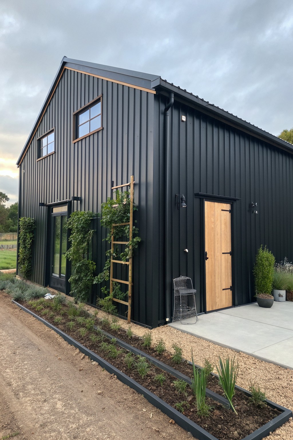 A small black metal barndominium with wood accents on the door and window frames, plus a long raised garden bed along the front.