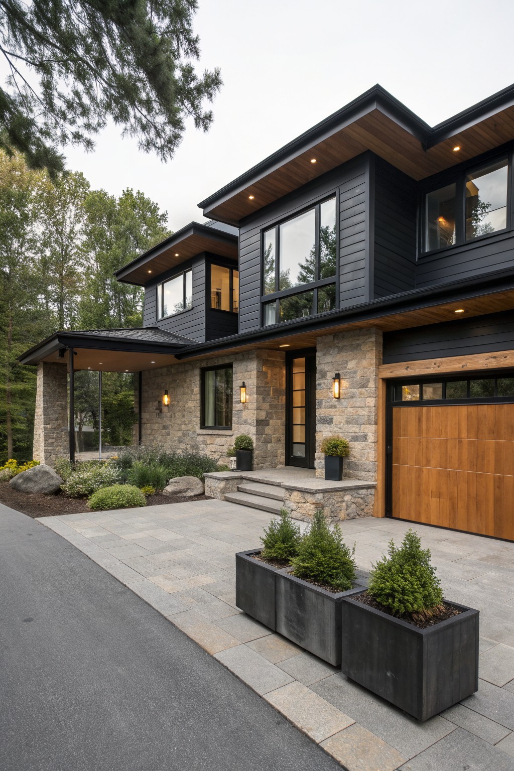 A modern two-story house with black siding, stone walls, a wooden garage door, and concrete planters along the driveway.