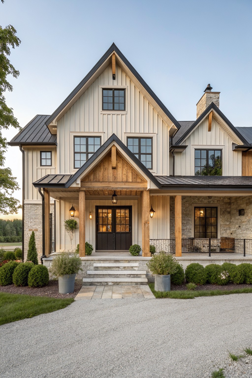 Front view of a two-story modern farmhouse with a central gable, stone lower walls, white vertical siding, wooden porch columns, black metal roof, and double front doors with grid windows.