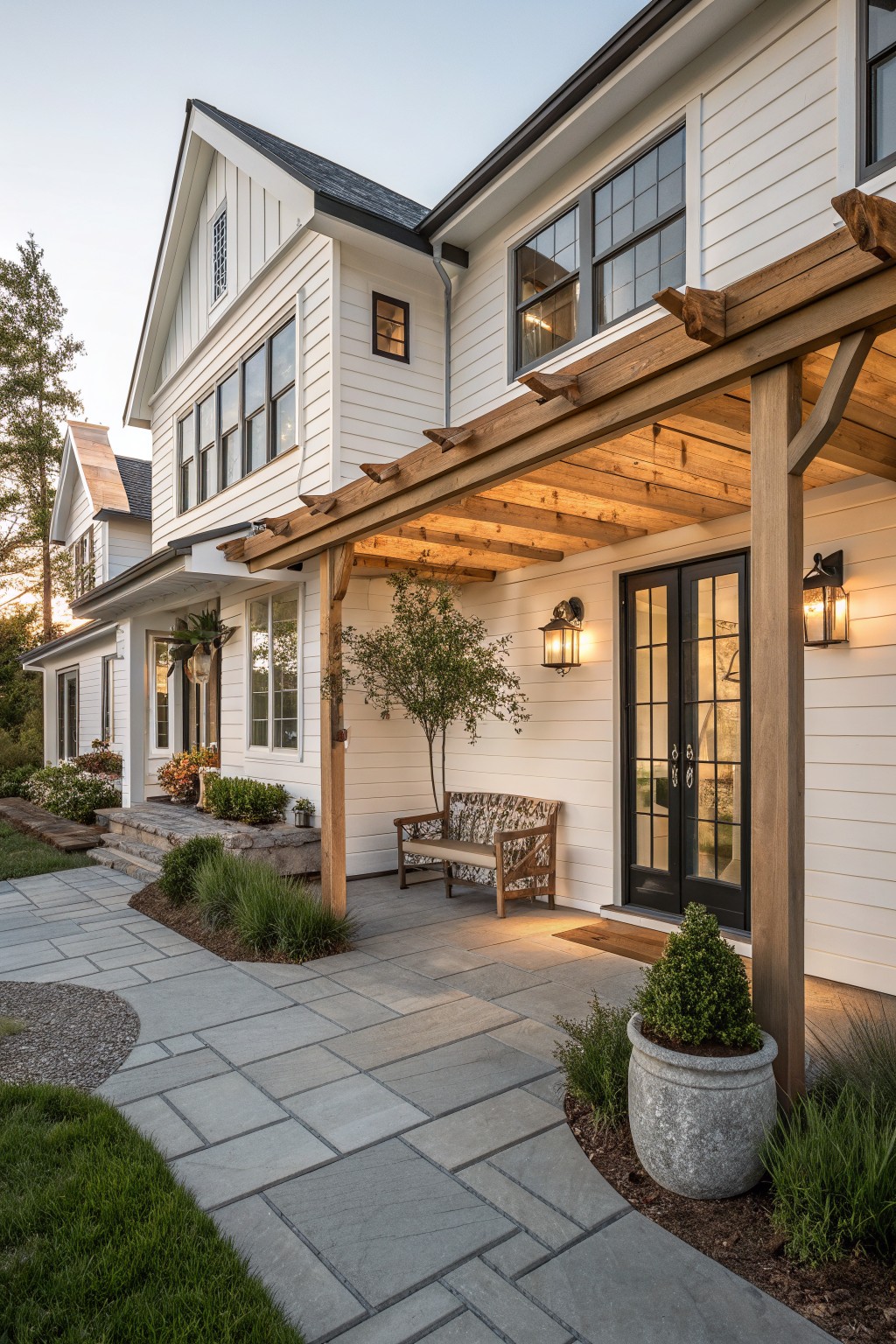 White farmhouse exterior with a wooden pergola covering the front porch, black double doors, and stone pavers leading to the entry.